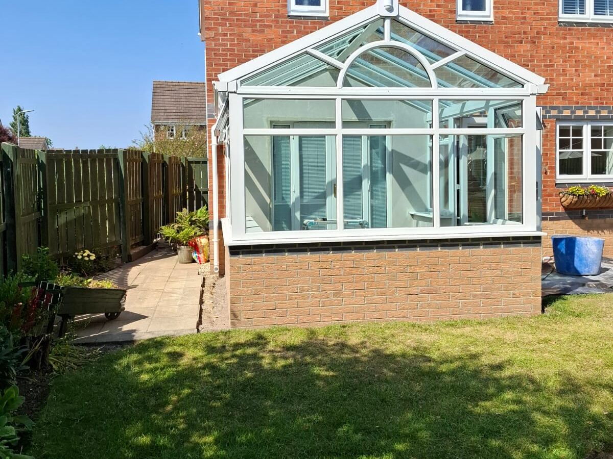A white Victorian style conservatory attached to a brick house